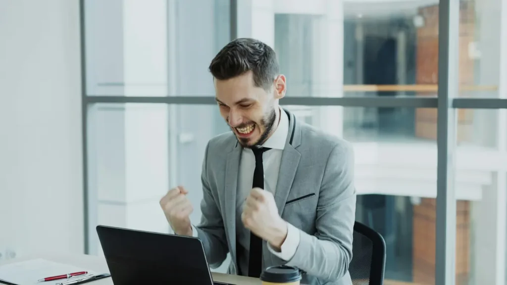 Professionnel célébrant une réussite devant son ordinateur : la relation client comme avantage concurrentiel